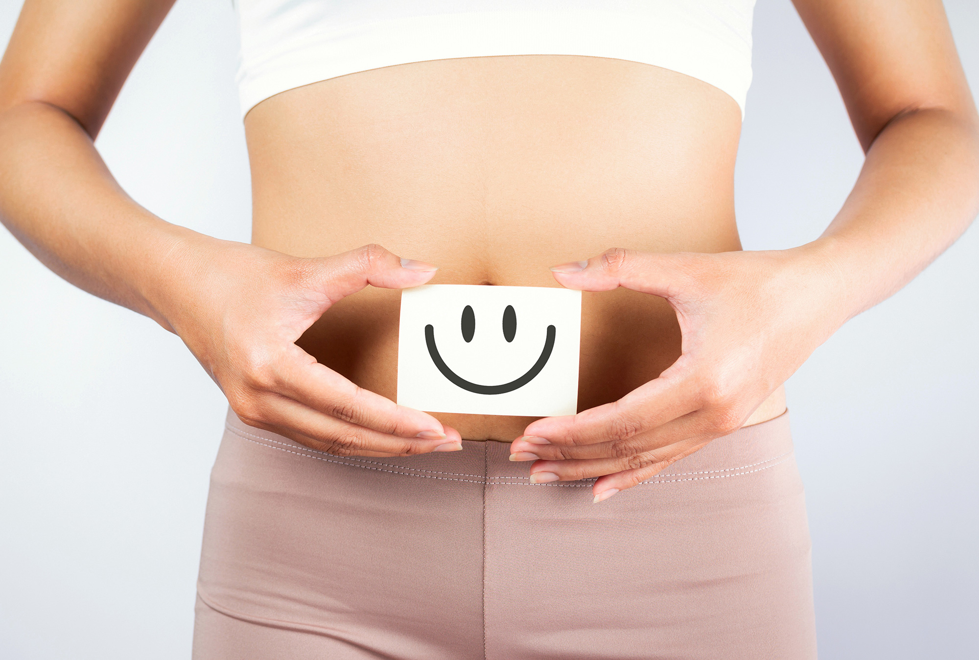 Photo of a woman holding a small piece of paper with a smiley face drawn on it over her bare abdomen.
